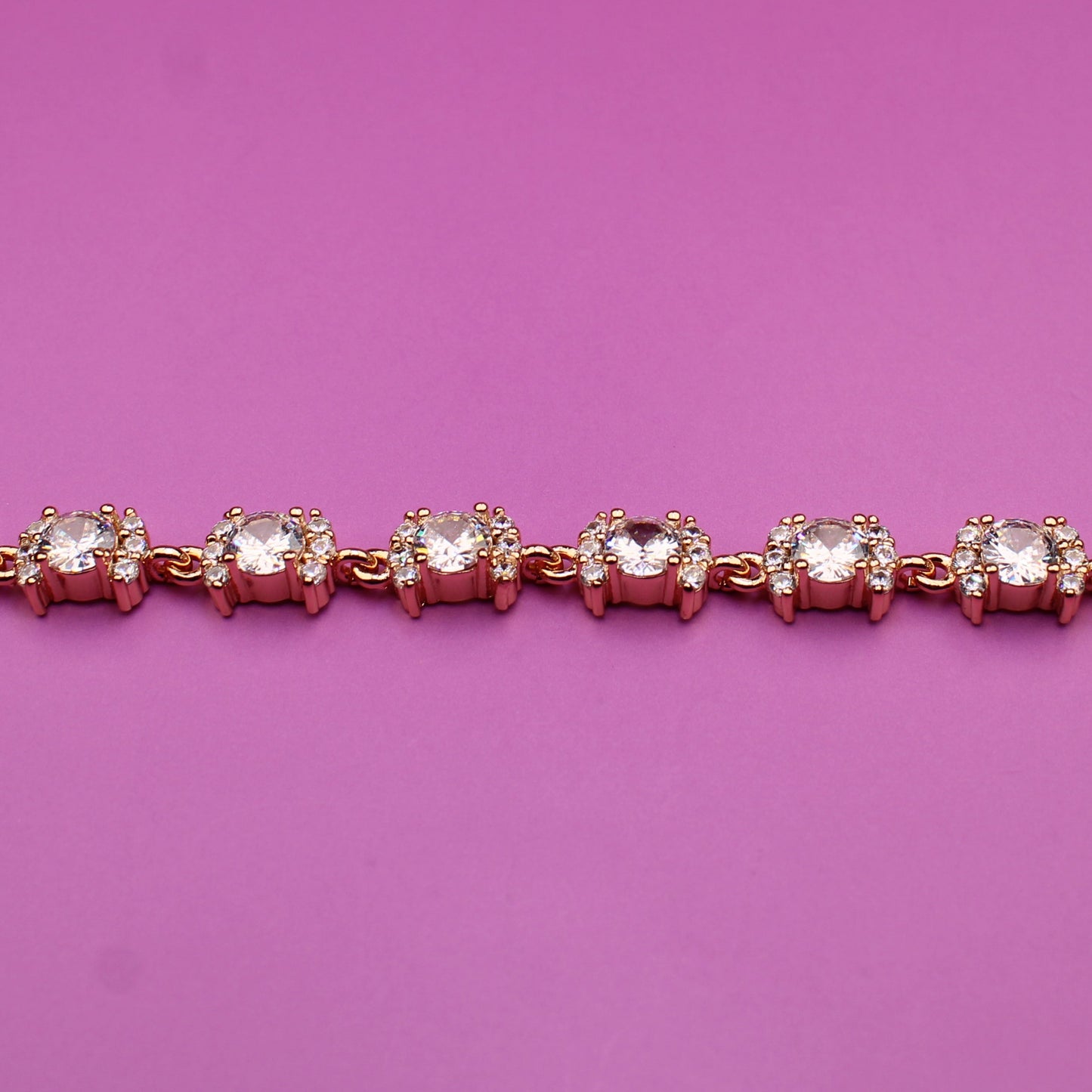 Rose gold bracelet with clear stones on a pink background