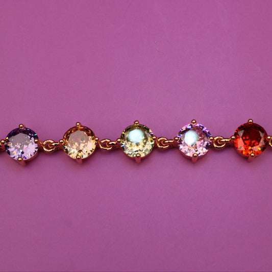 Gold bracelet with multicolored gemstones on a pink background