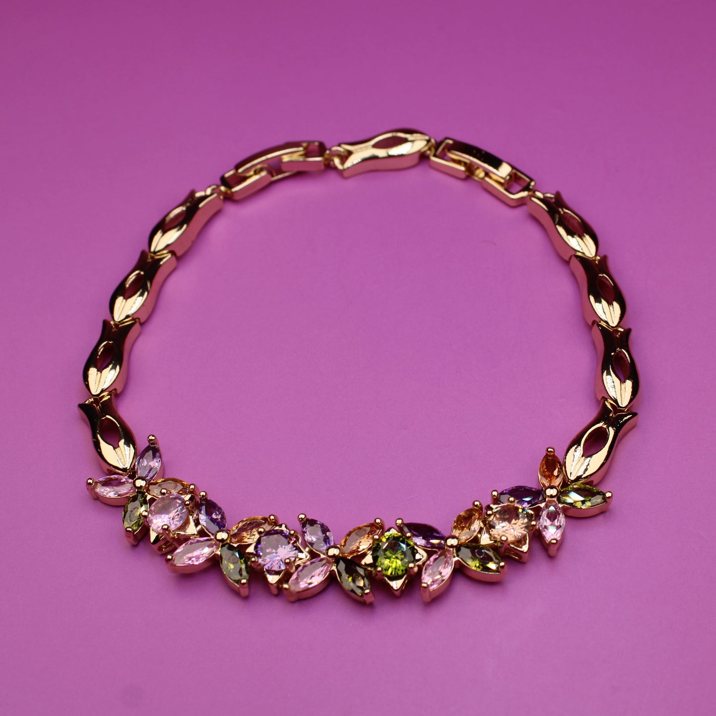 Gold bracelet with colorful gemstones on a pink background