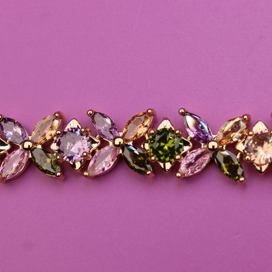Gold bracelet with multicolored gemstones on a pink background