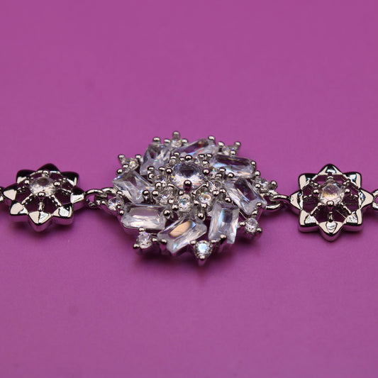Silver bracelet with floral designs and clear stones on a purple background