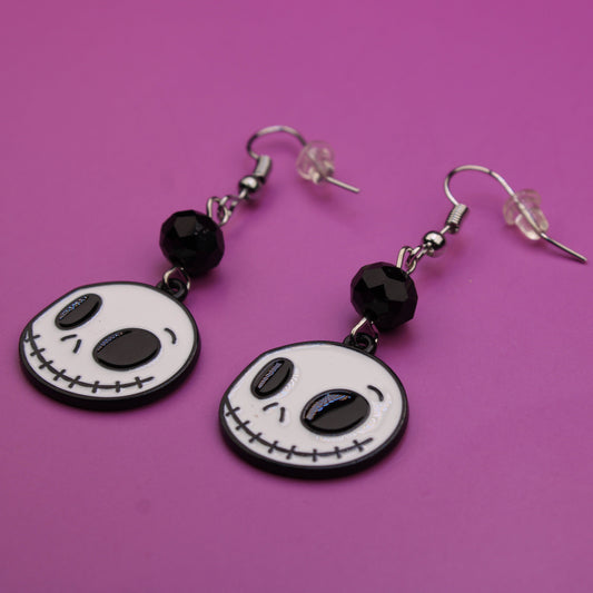 Skull-shaped earrings with black beads on a purple background