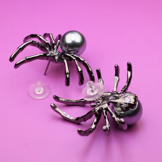 Two spider-shaped earrings on a pink background
