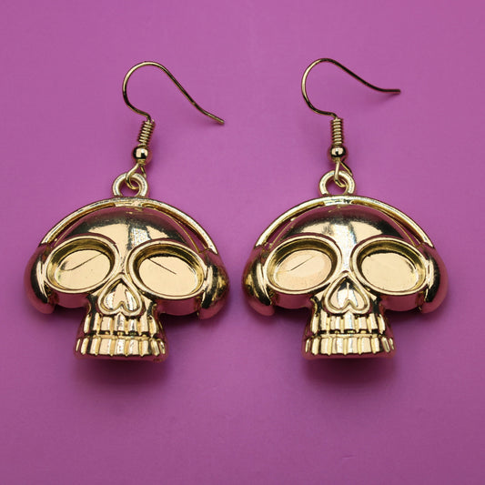 Gold skull-shaped earrings on a purple background