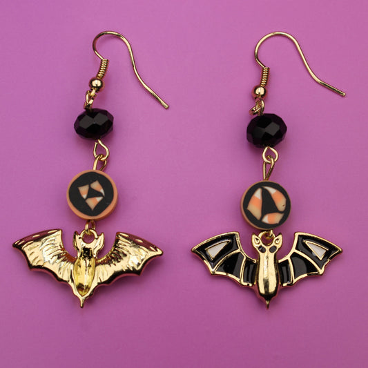 Bat-shaped earrings with black beads on a purple background