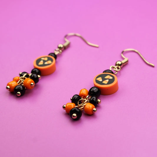 Halloween-themed earrings with pumpkin designs on a pink background