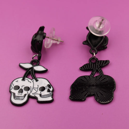 Pair of earrings with skull and bow design on a pink background