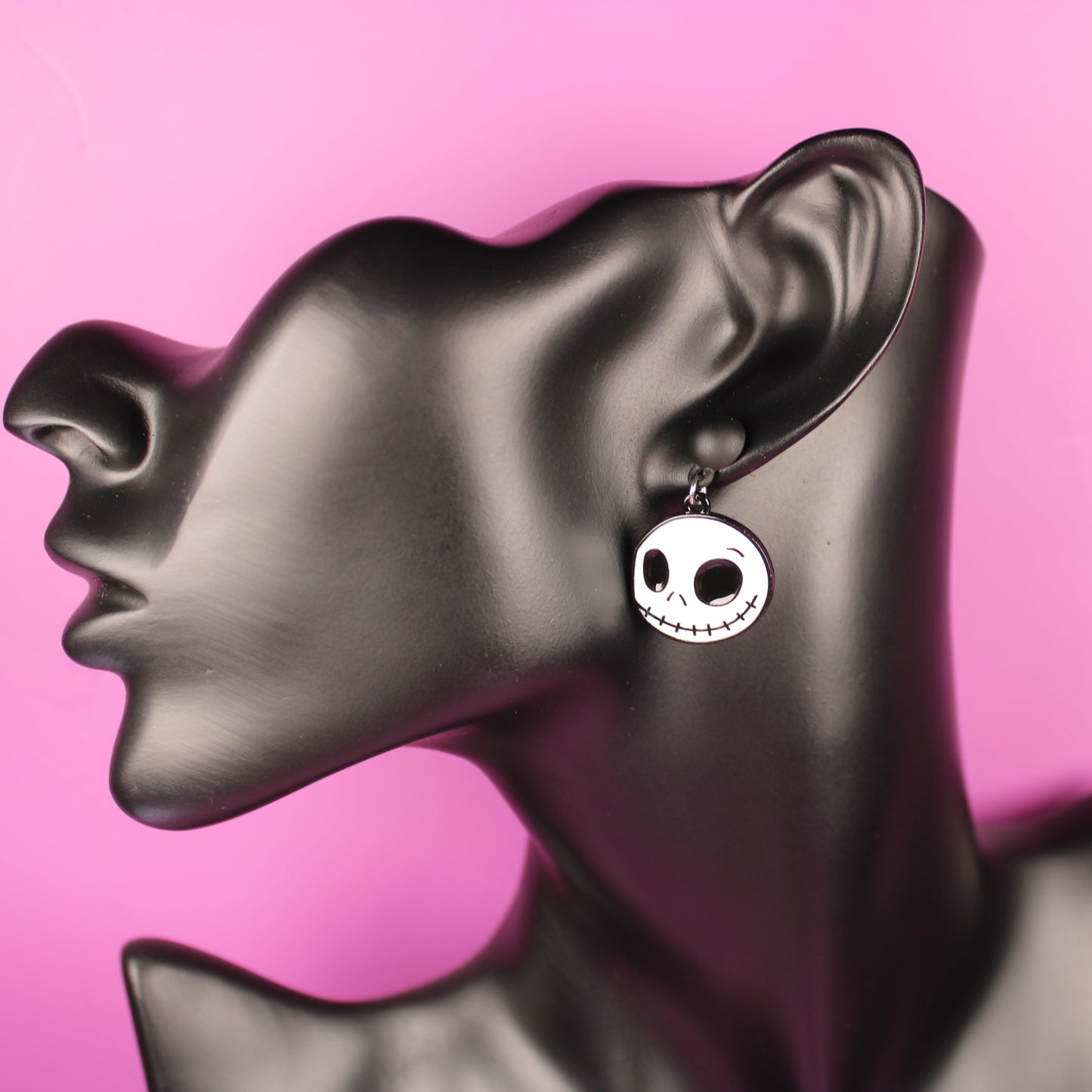 Skull-shaped earrings on a mannequin bust with a pink background