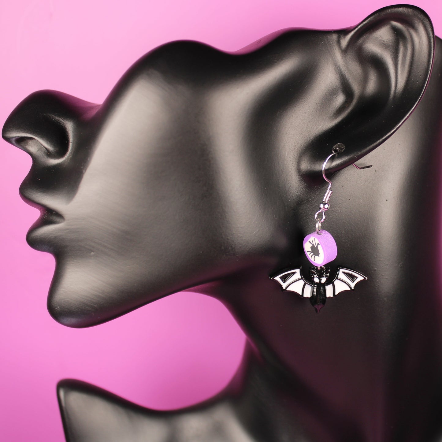 Bat-shaped earring on a black mannequin head with pink background