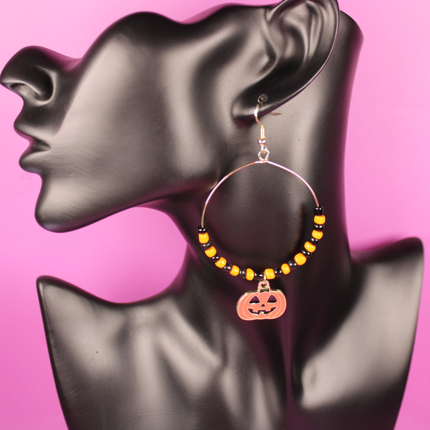 Halloween-themed hoop earrings on a mannequin bust with a pink background