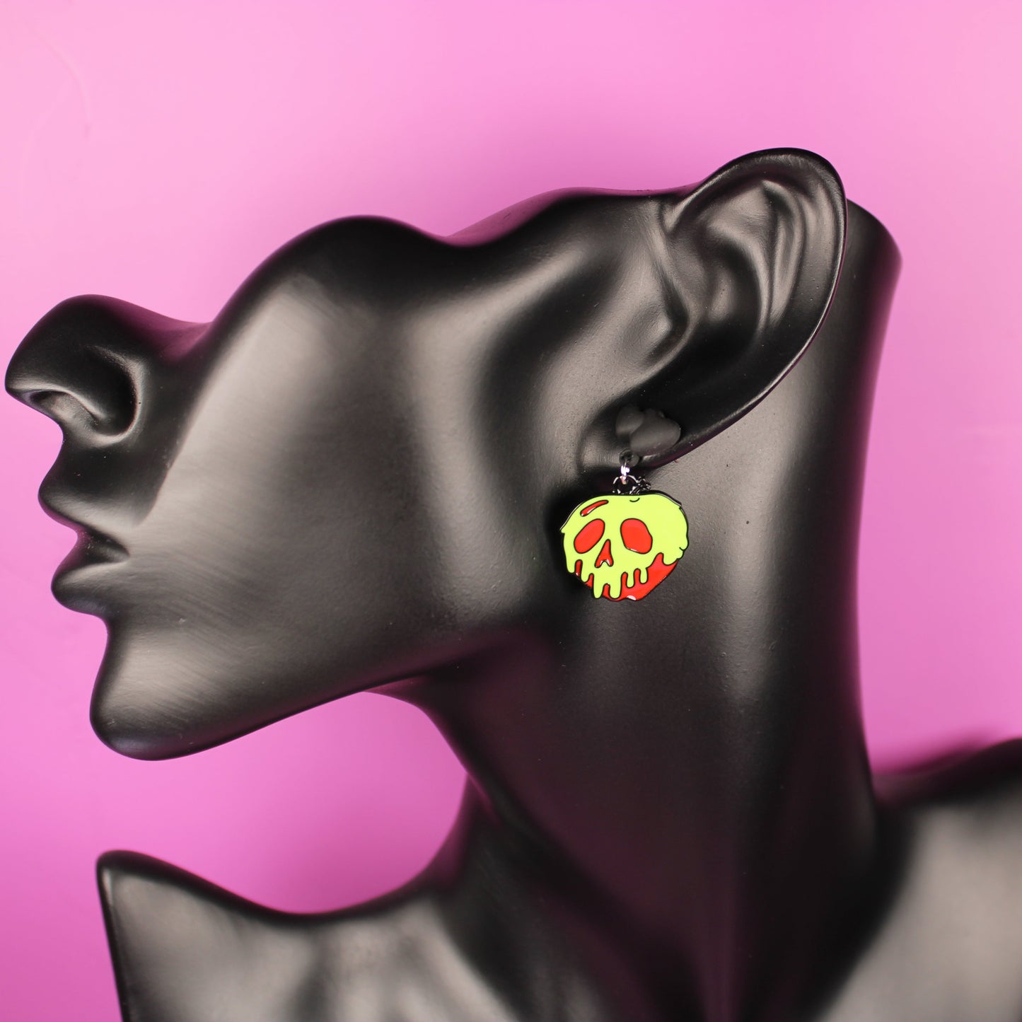 Black mannequin head with colorful skull-shaped earrings on a pink background