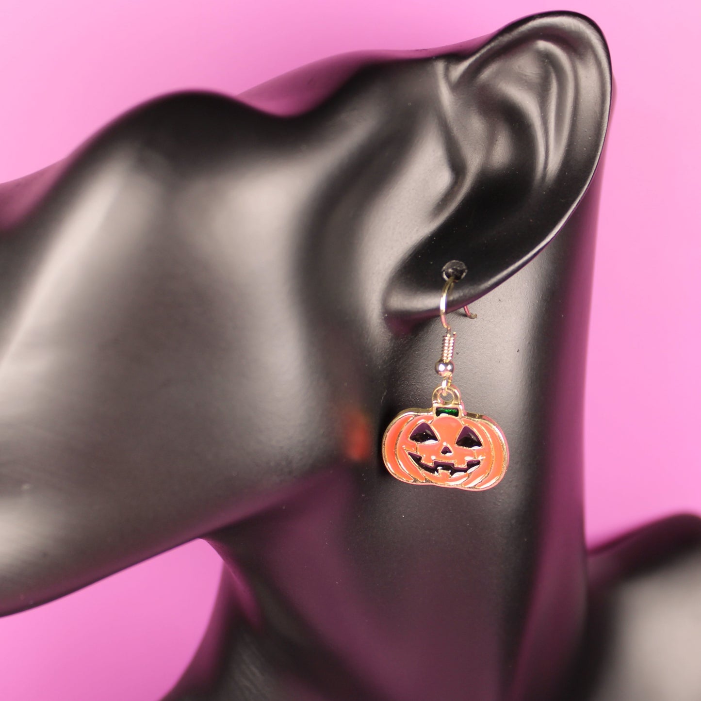 Halloween-themed pumpkin earrings on a mannequin ear with a pink background