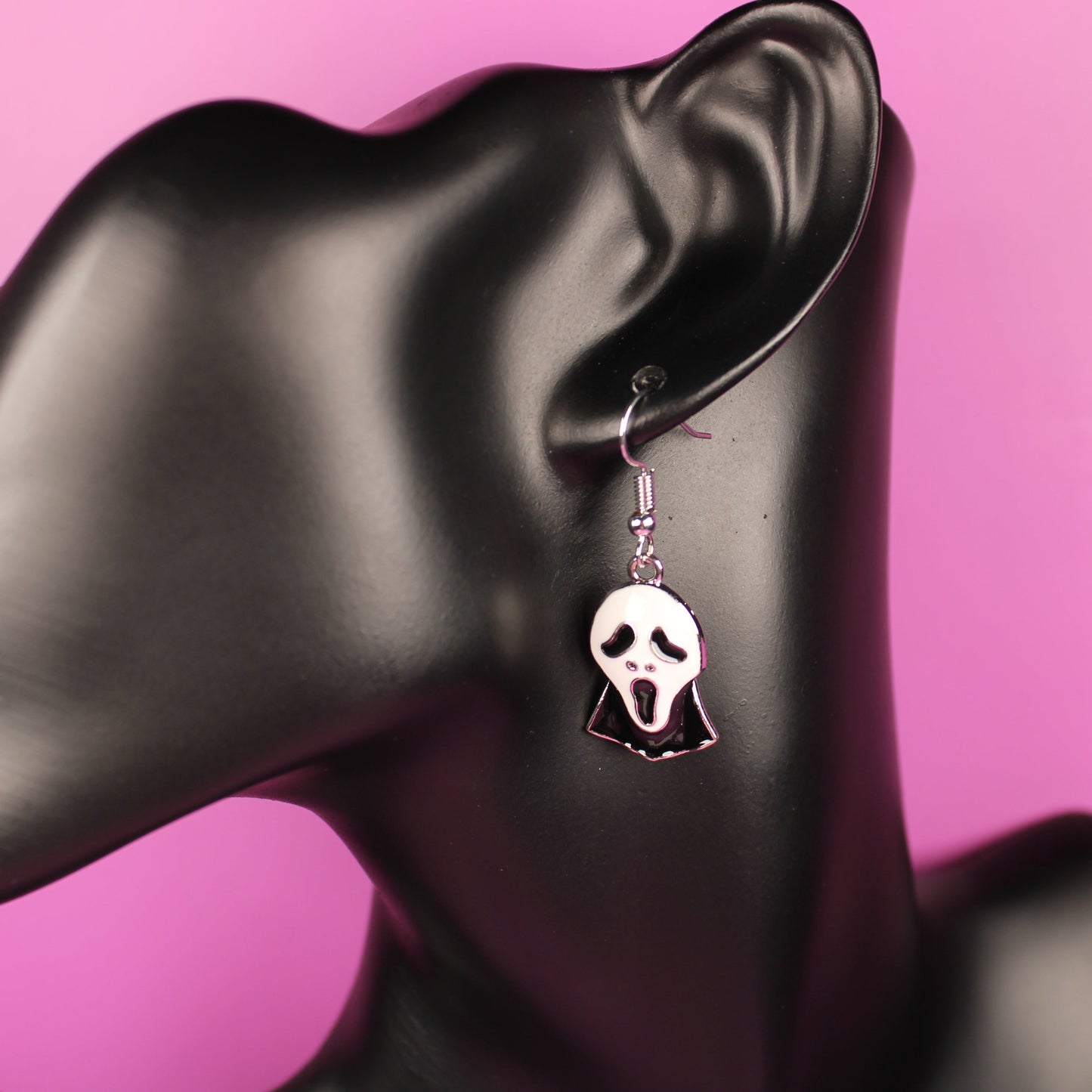 Earring with a skull design on a black mannequin against a pink background