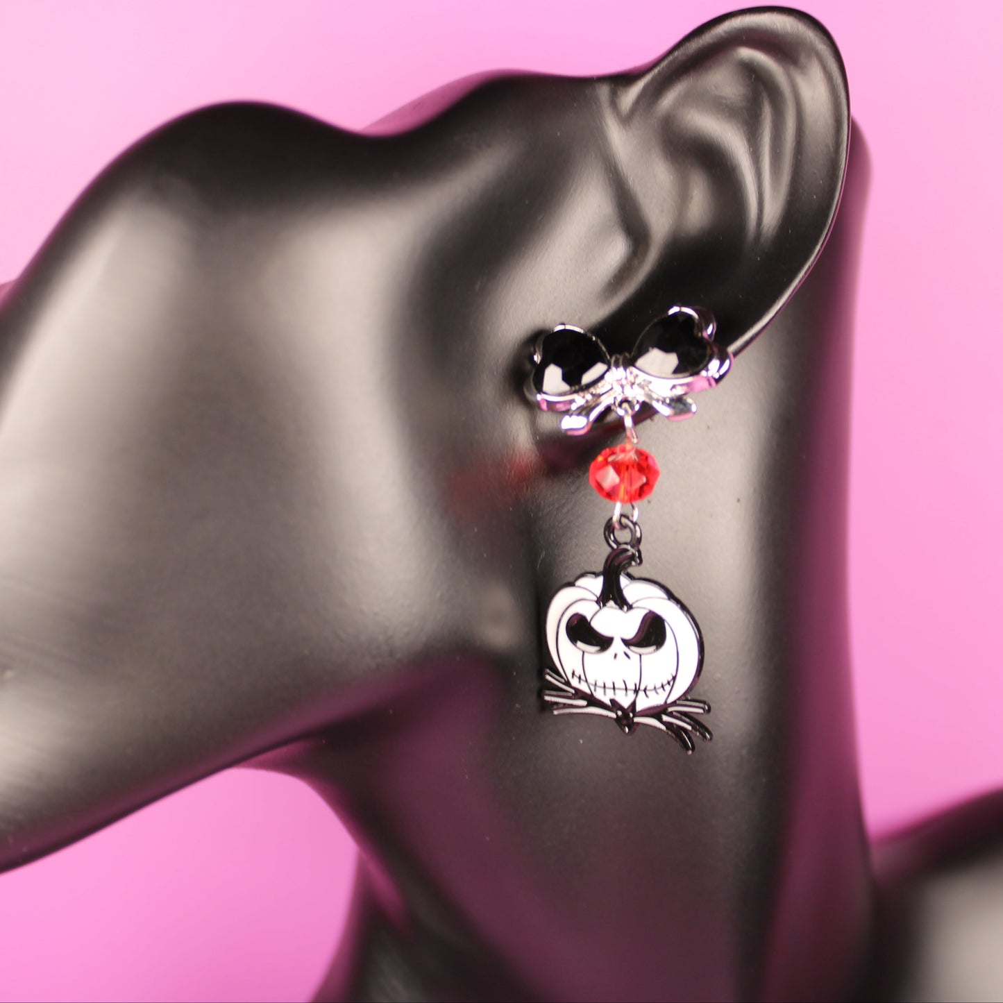 Earring with skull design on a gray mannequin head against a pink background