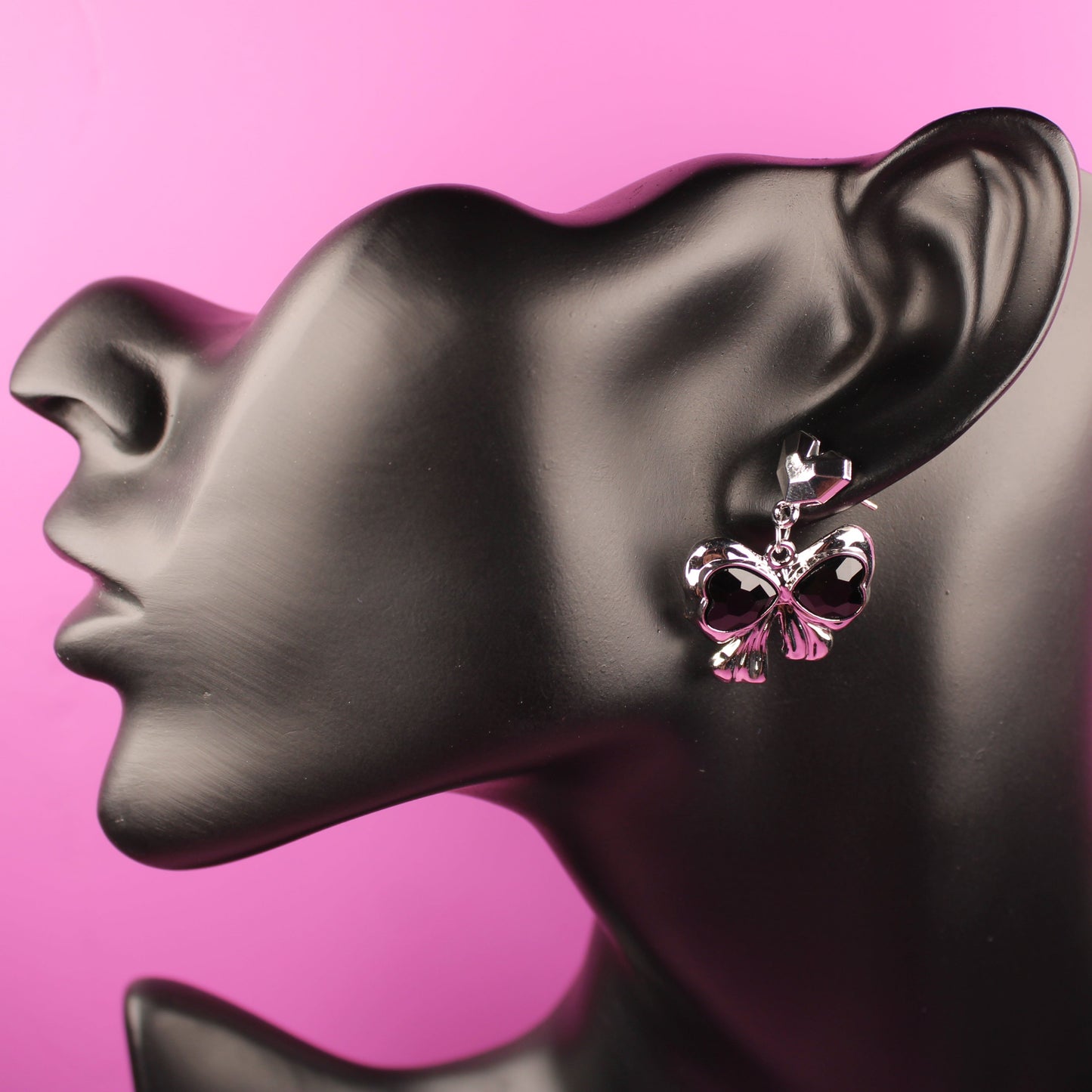 Butterfly-shaped earrings on a mannequin head with a pink background