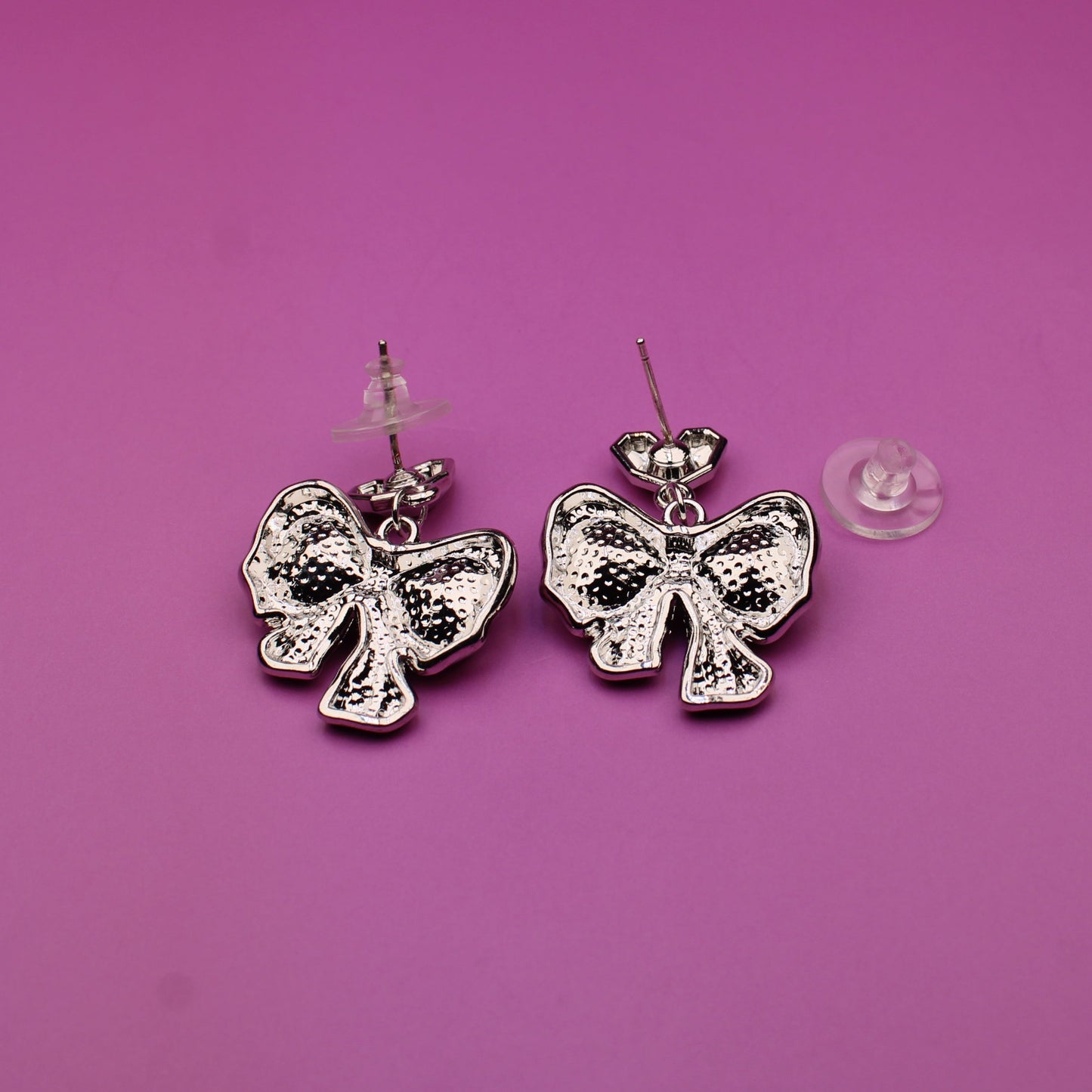 Silver bow-shaped earrings on a pink background