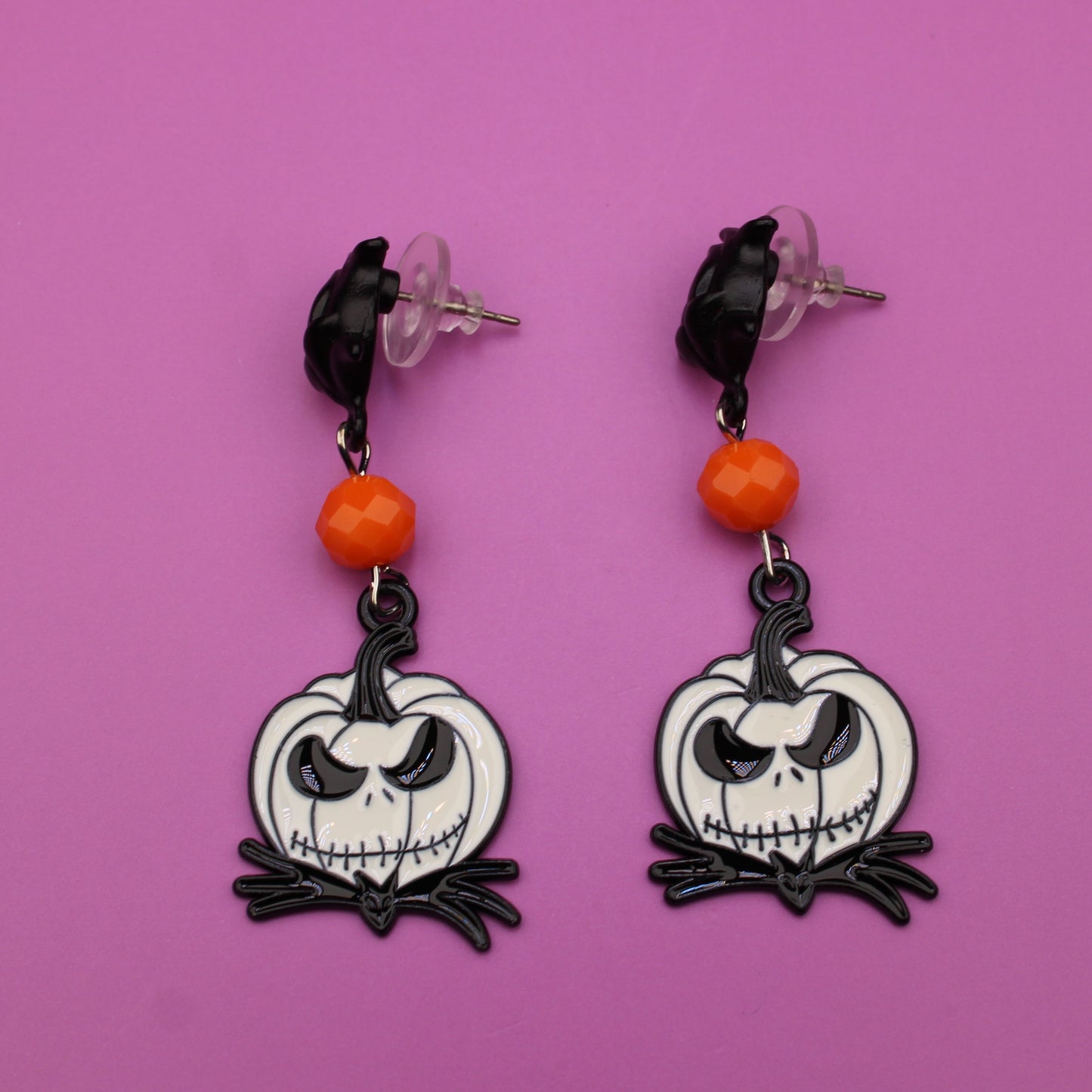 Pair of earrings with skull design on a pink background