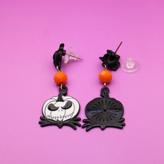 Halloween-themed earrings on a pink background