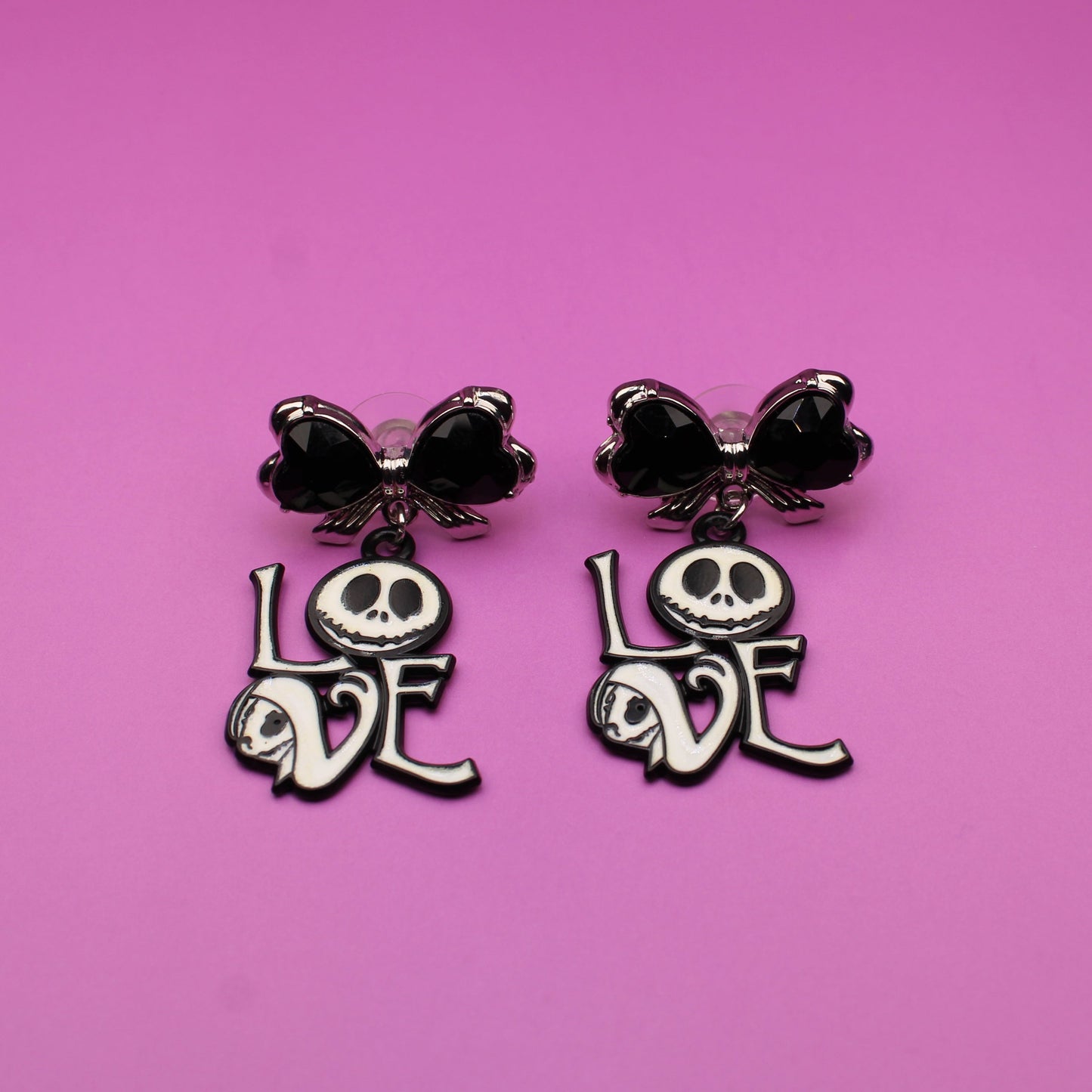Pair of earrings with skull designs and 'LOVE' text on a pink background