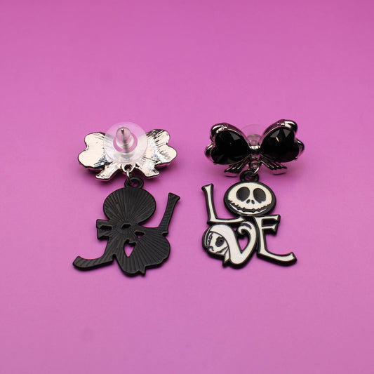 Two black and white earrings with decorative elements on a pink background