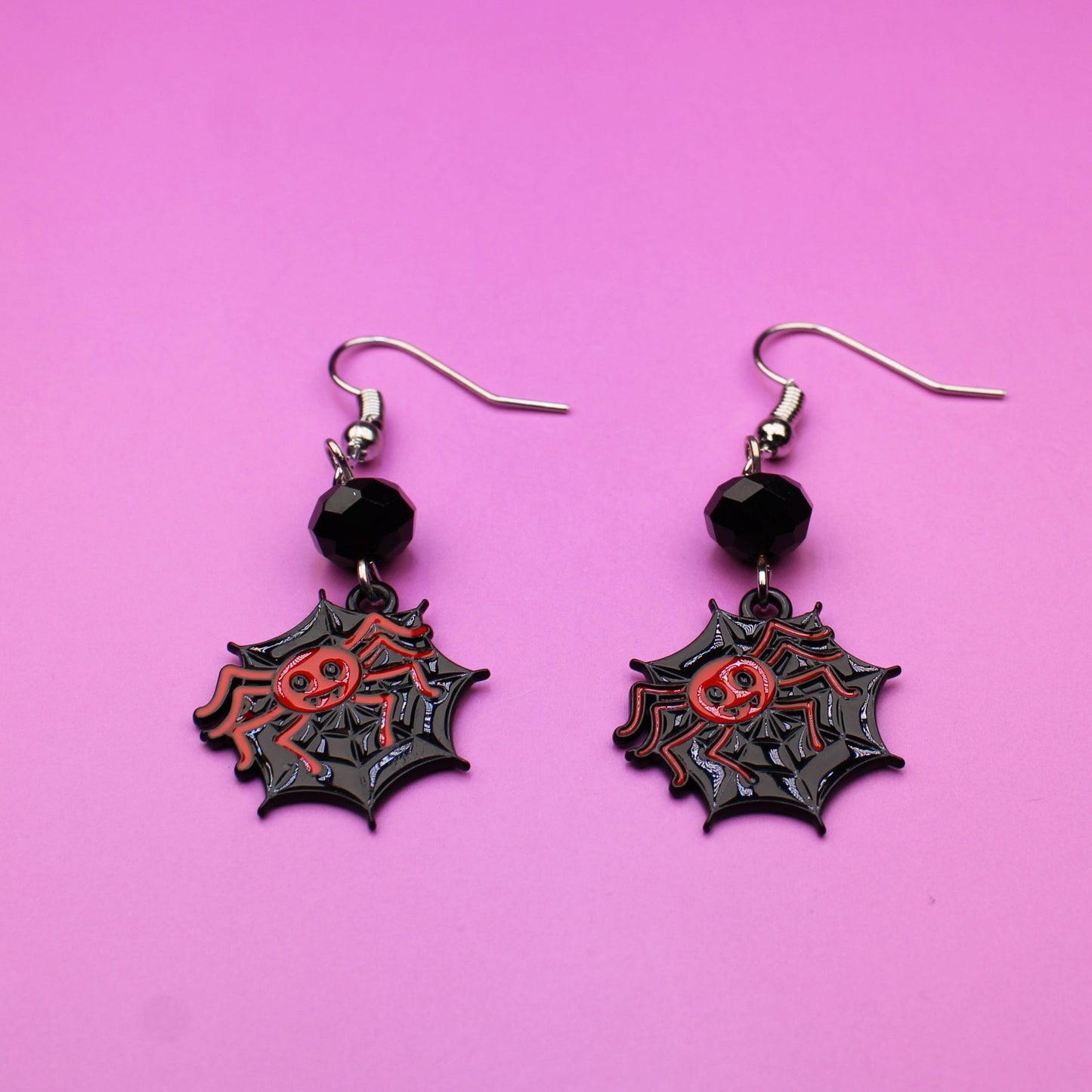 Pair of spider web earrings on a pink background