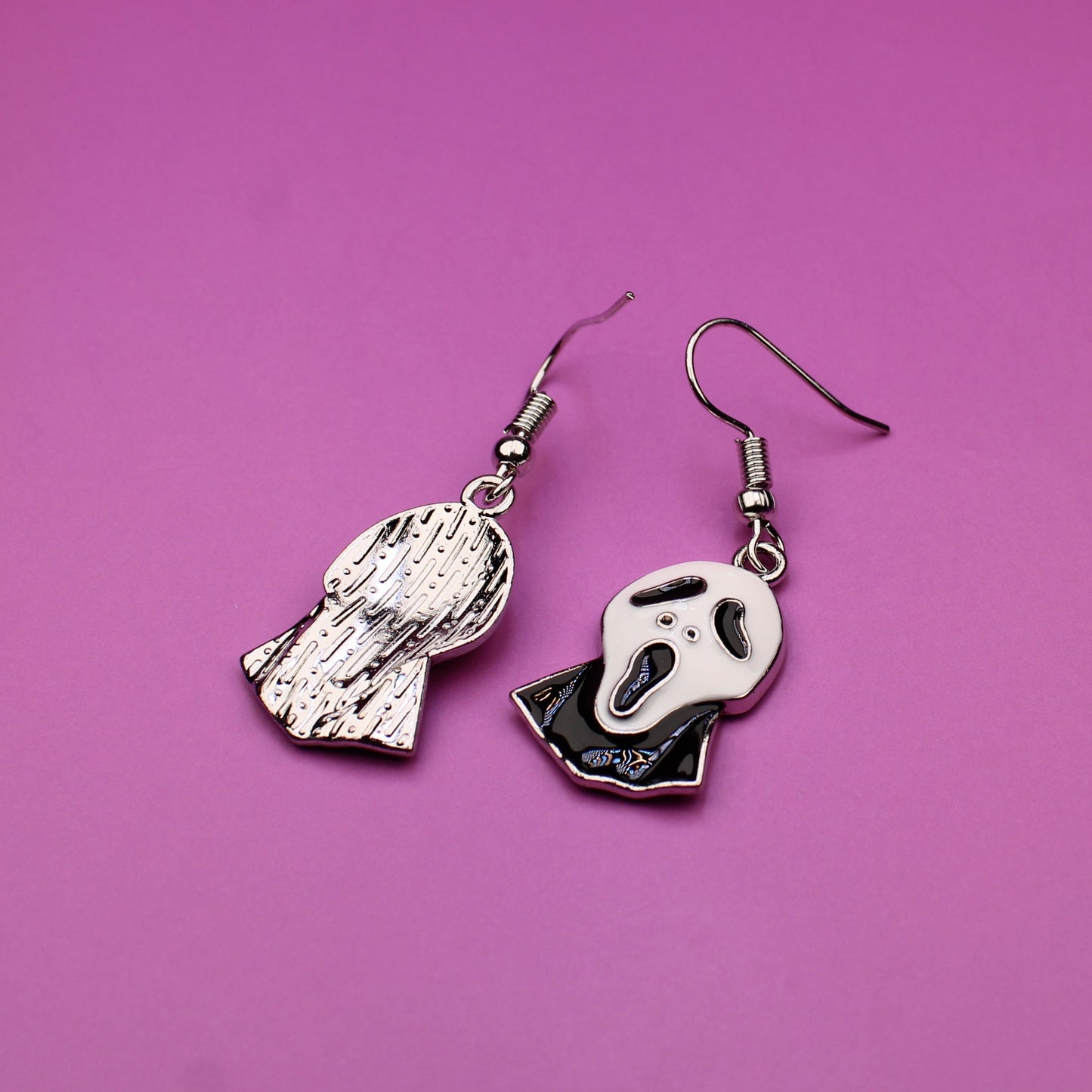 Pair of skeleton hand earrings on a pink background