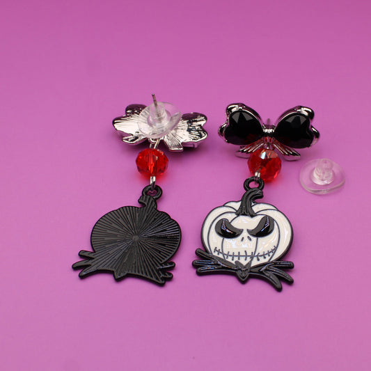 Two Halloween-themed earrings on a pink background
