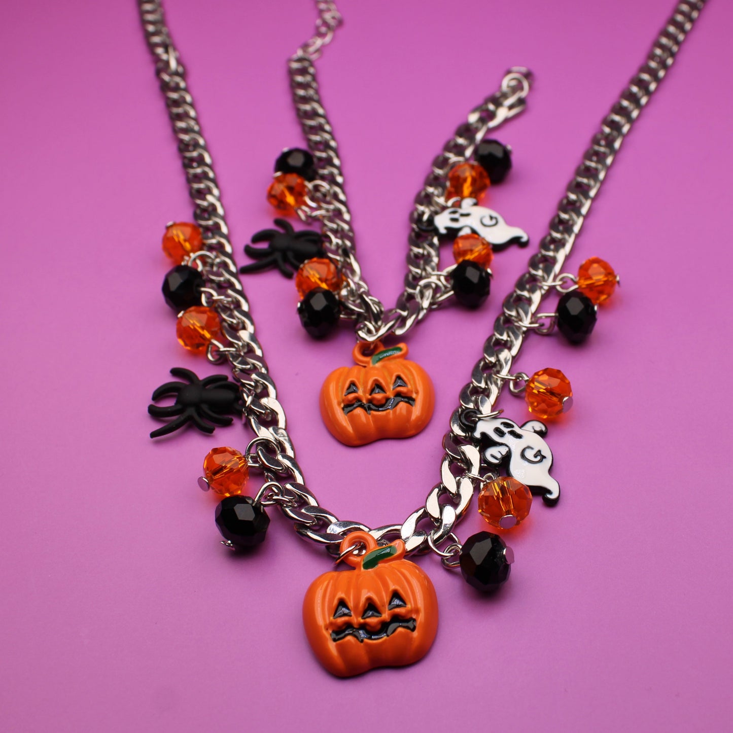 Halloween-themed necklace with pumpkin and spider charms on a pink background