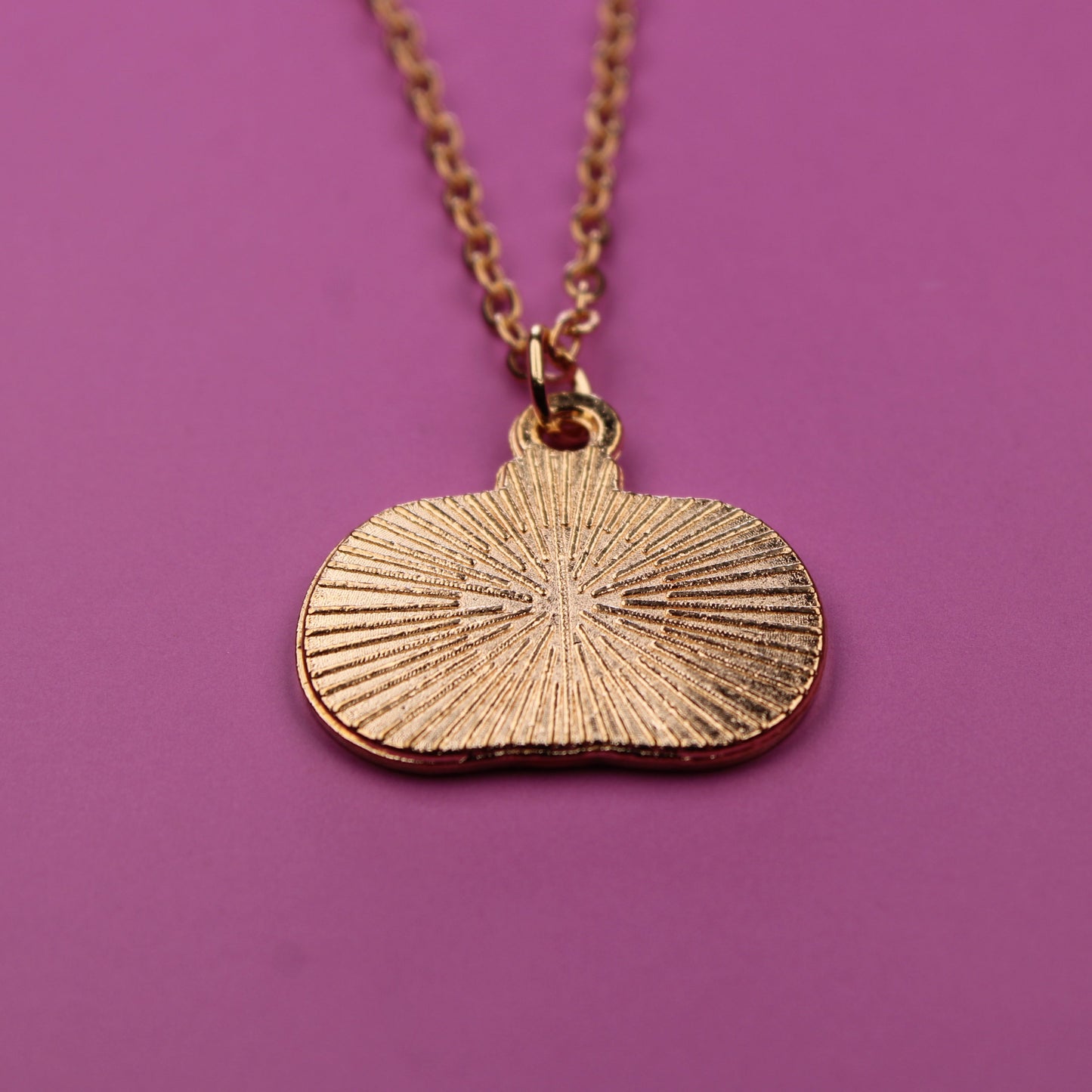 Gold necklace with a sunburst pendant on a purple background