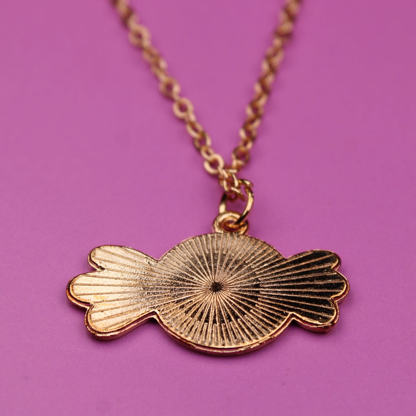 Gold necklace with a unique pendant on a pink background