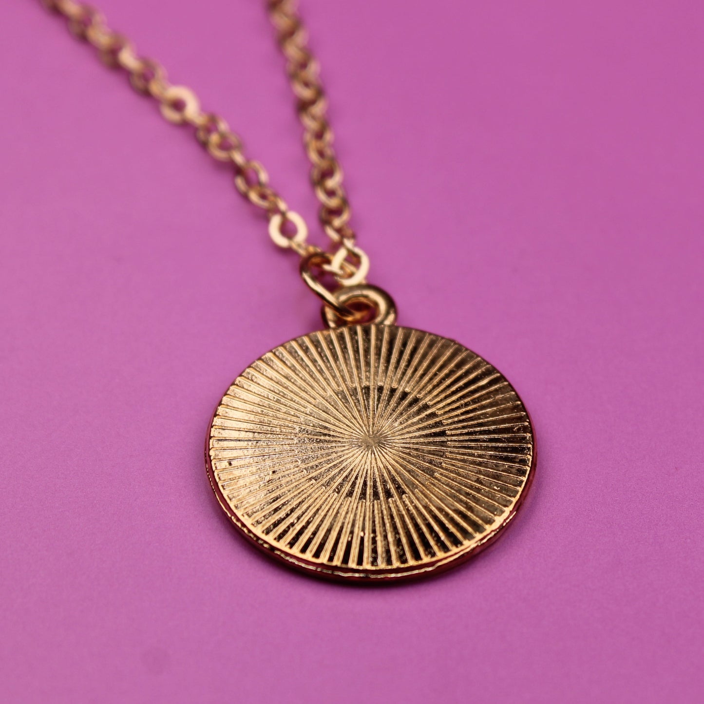 Gold necklace with a round pendant on a pink background