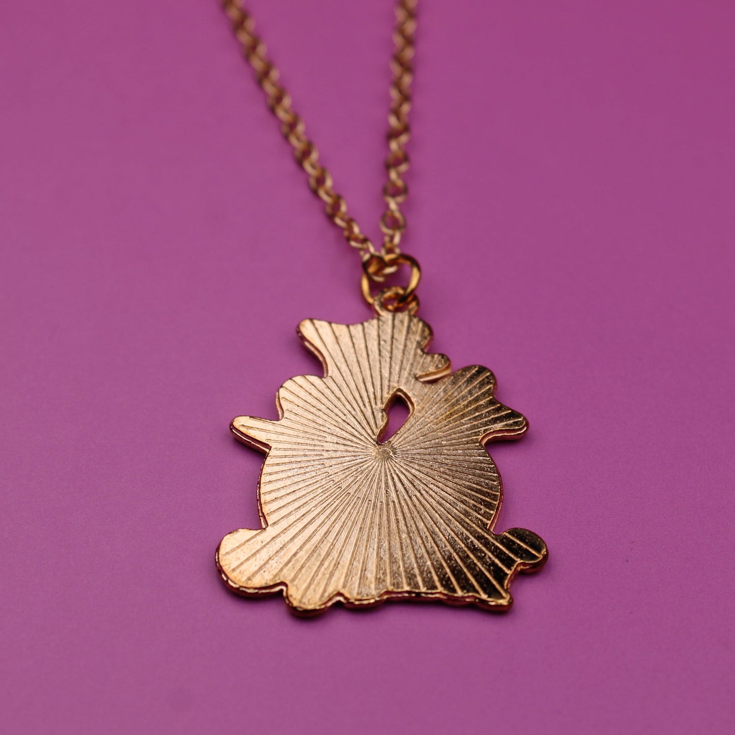 Gold necklace with a leaf-shaped pendant on a purple background