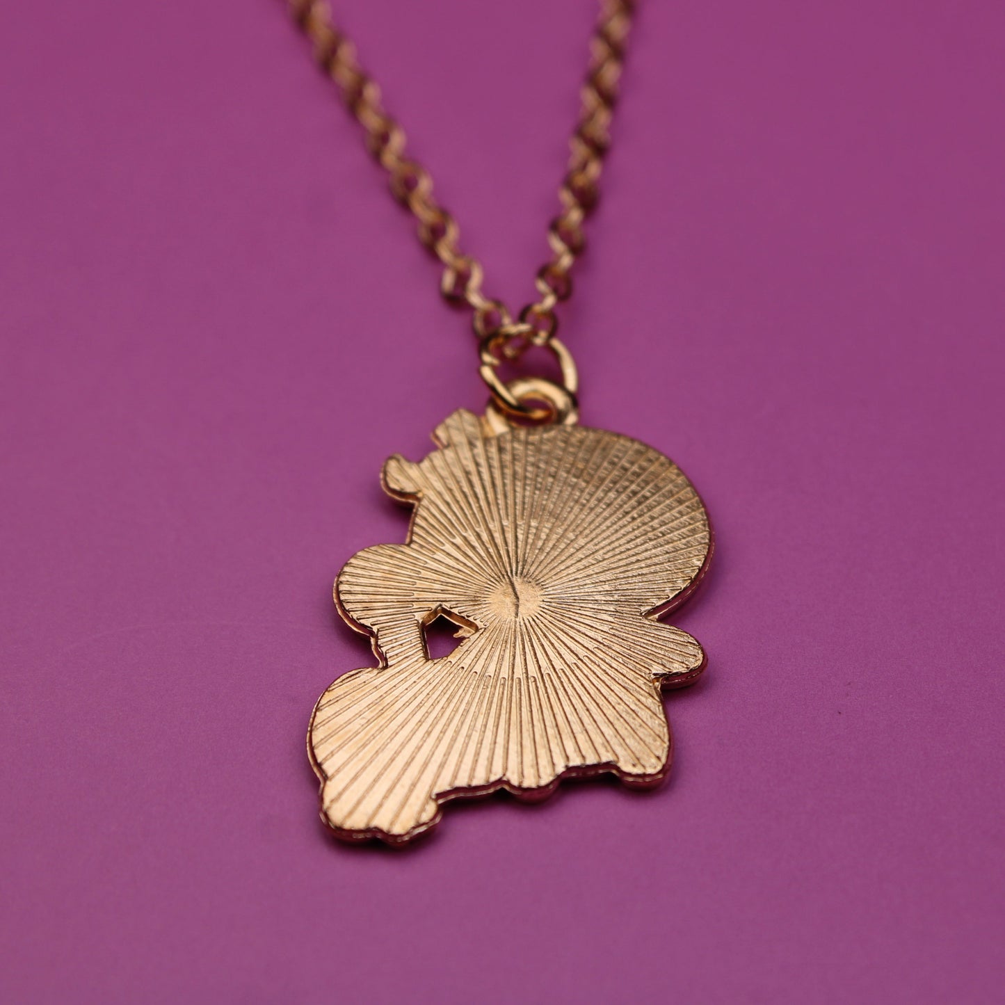 Gold necklace with a leaf-shaped pendant on a purple background