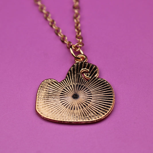 Gold necklace with a heart-shaped pendant on a pink background