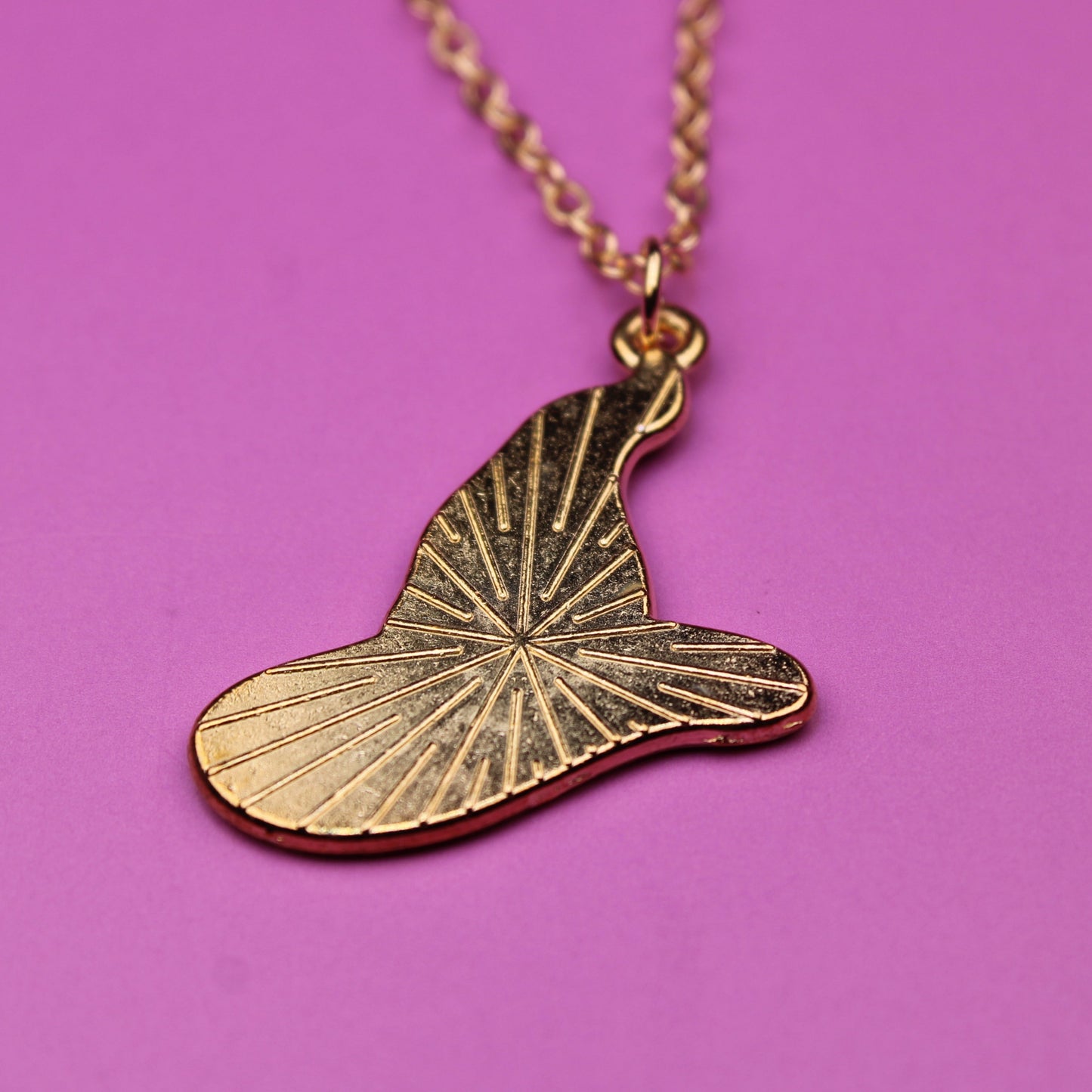 Gold leaf-shaped pendant on a chain against a pink background