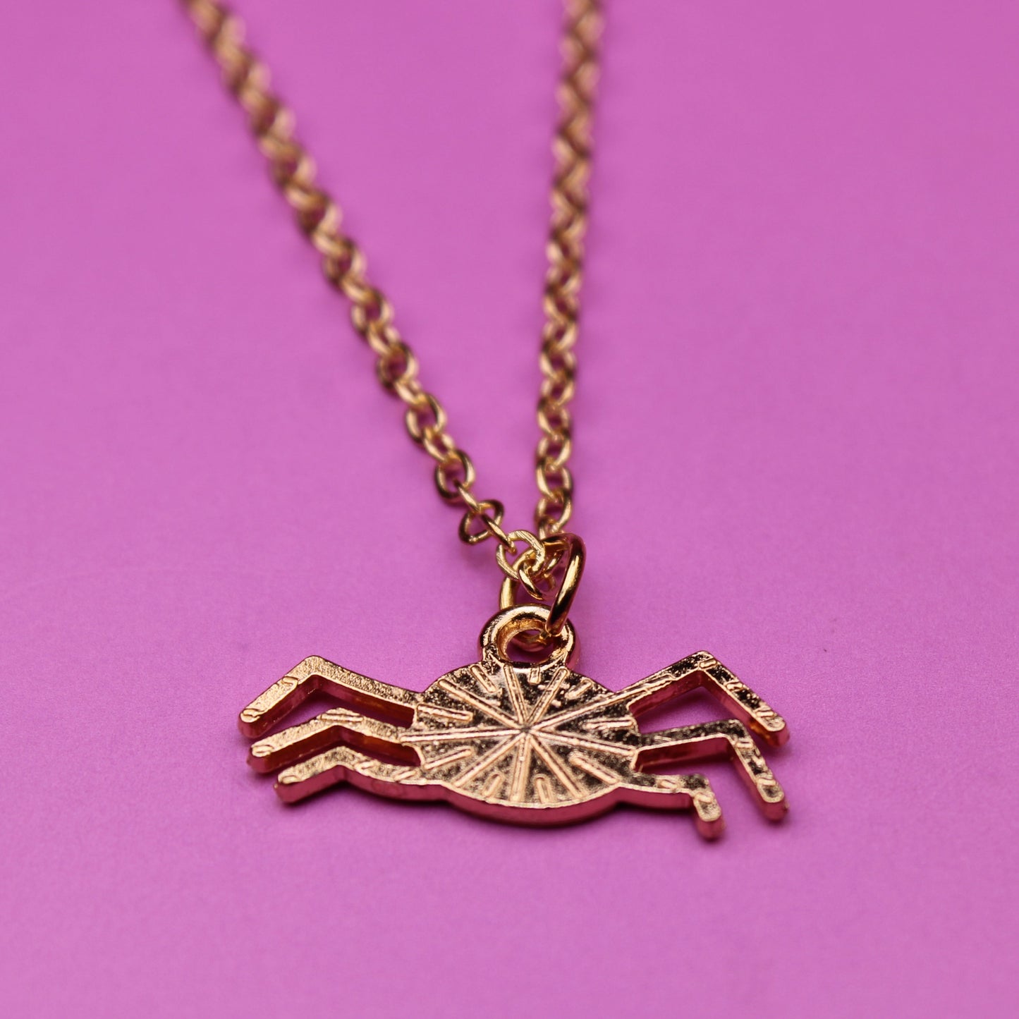 Gold crab-shaped pendant on a chain against a pink background