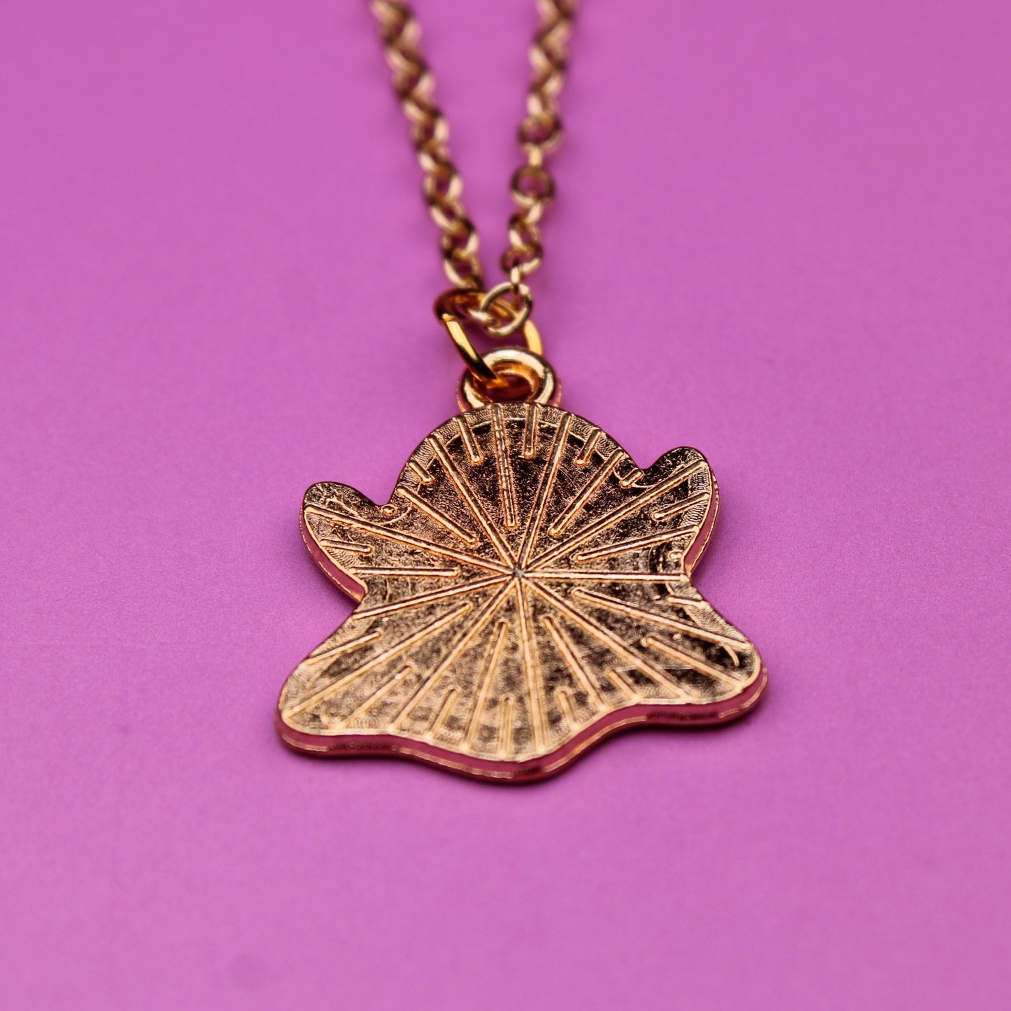 Gold necklace with a leaf-shaped pendant on a pink background