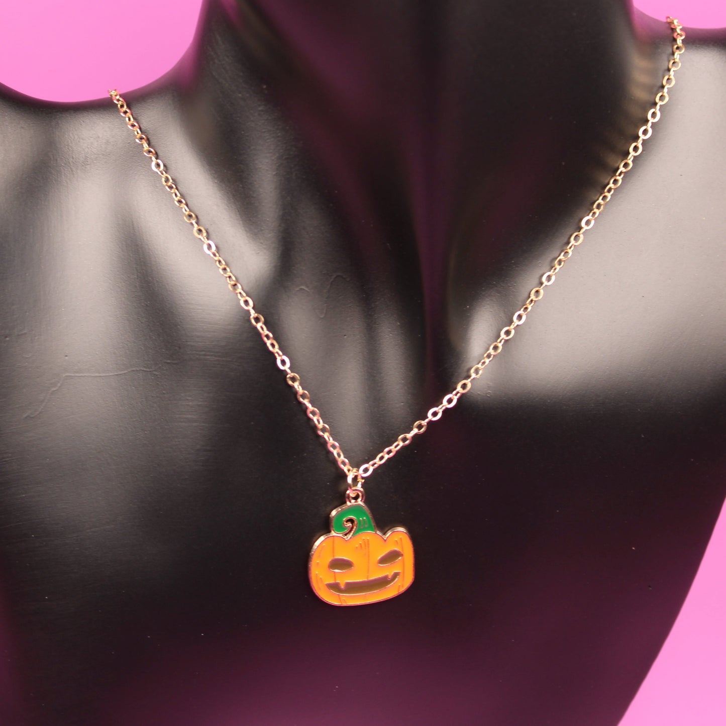 Necklace with a pumpkin pendant on a black mannequin bust against a pink background