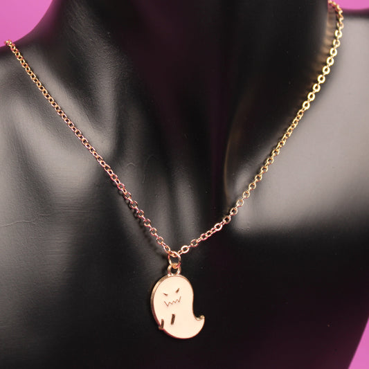Gold necklace with a ghost pendant on a black mannequin bust against a pink background