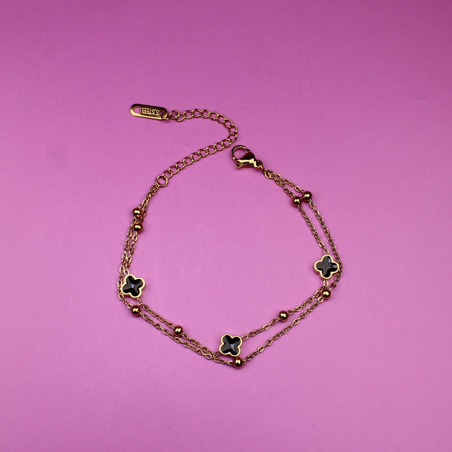 Gold bracelet with clover-shaped charms on a pink background
