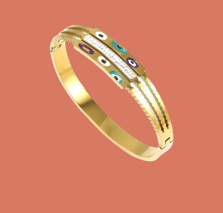 A 14K gold plated steel bangle bracelet with a hinged closure, featuring a gold finish, diamond-like sparkle, and a vibrant eye charm.