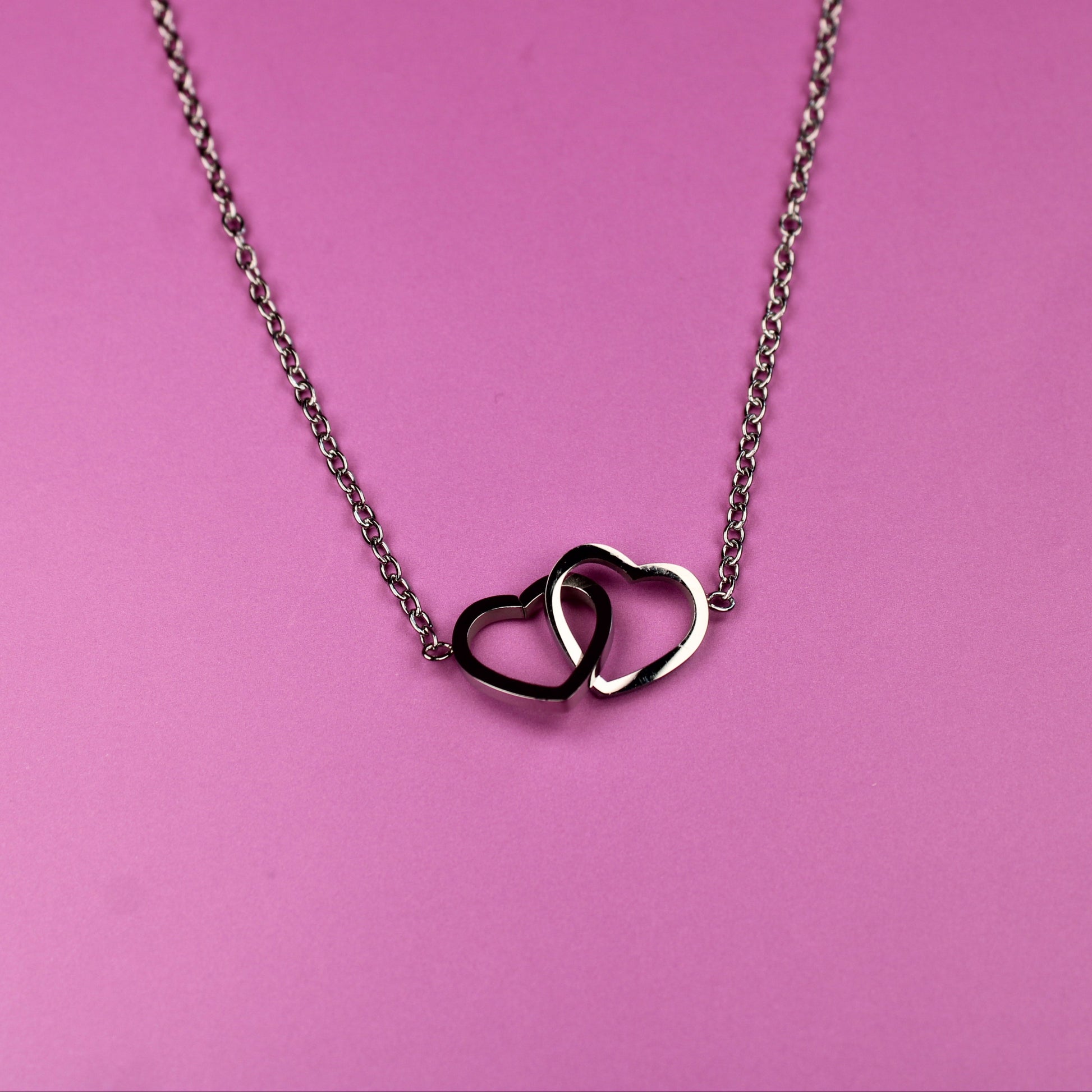 Necklace with interlocking heart pendants on a pink background