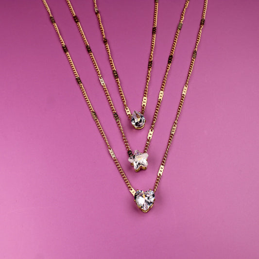 Three gold necklaces with star pendants on a pink background
