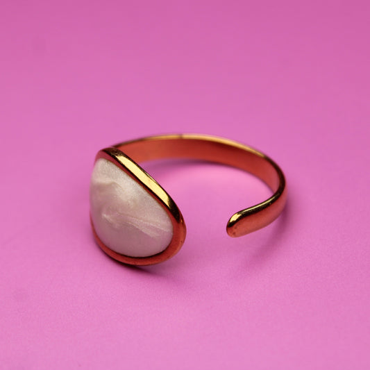 Gold ring with a white stone on a pink background