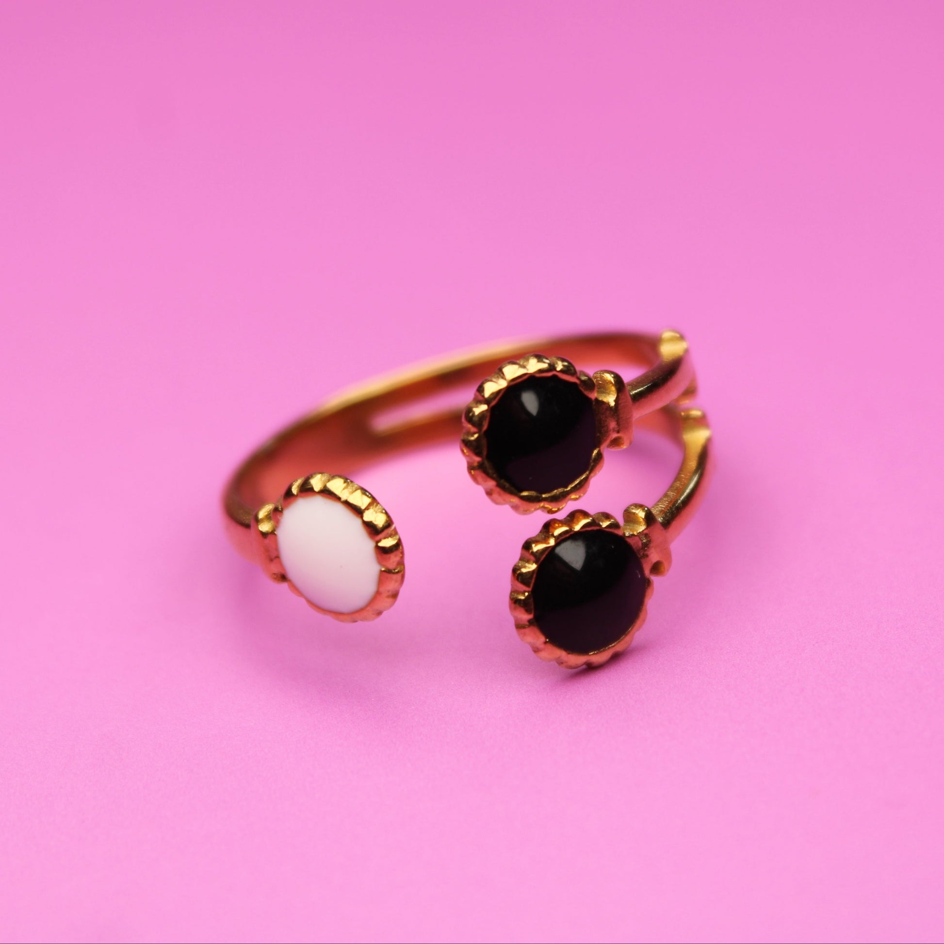 Gold ring with black and white gemstones on a pink background