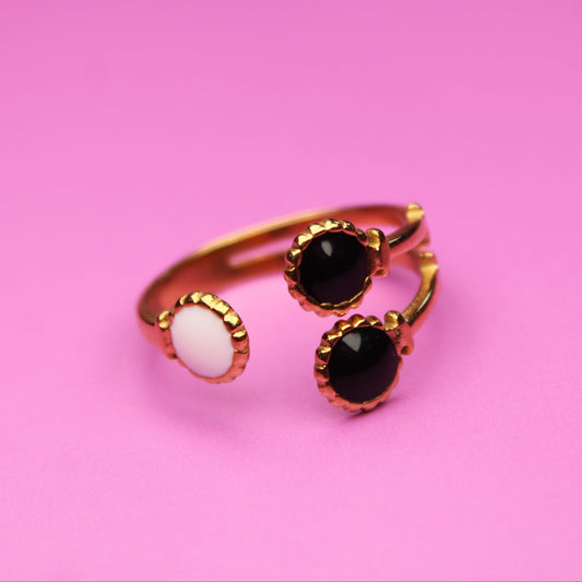 Gold ring with black and white gemstones on a pink background