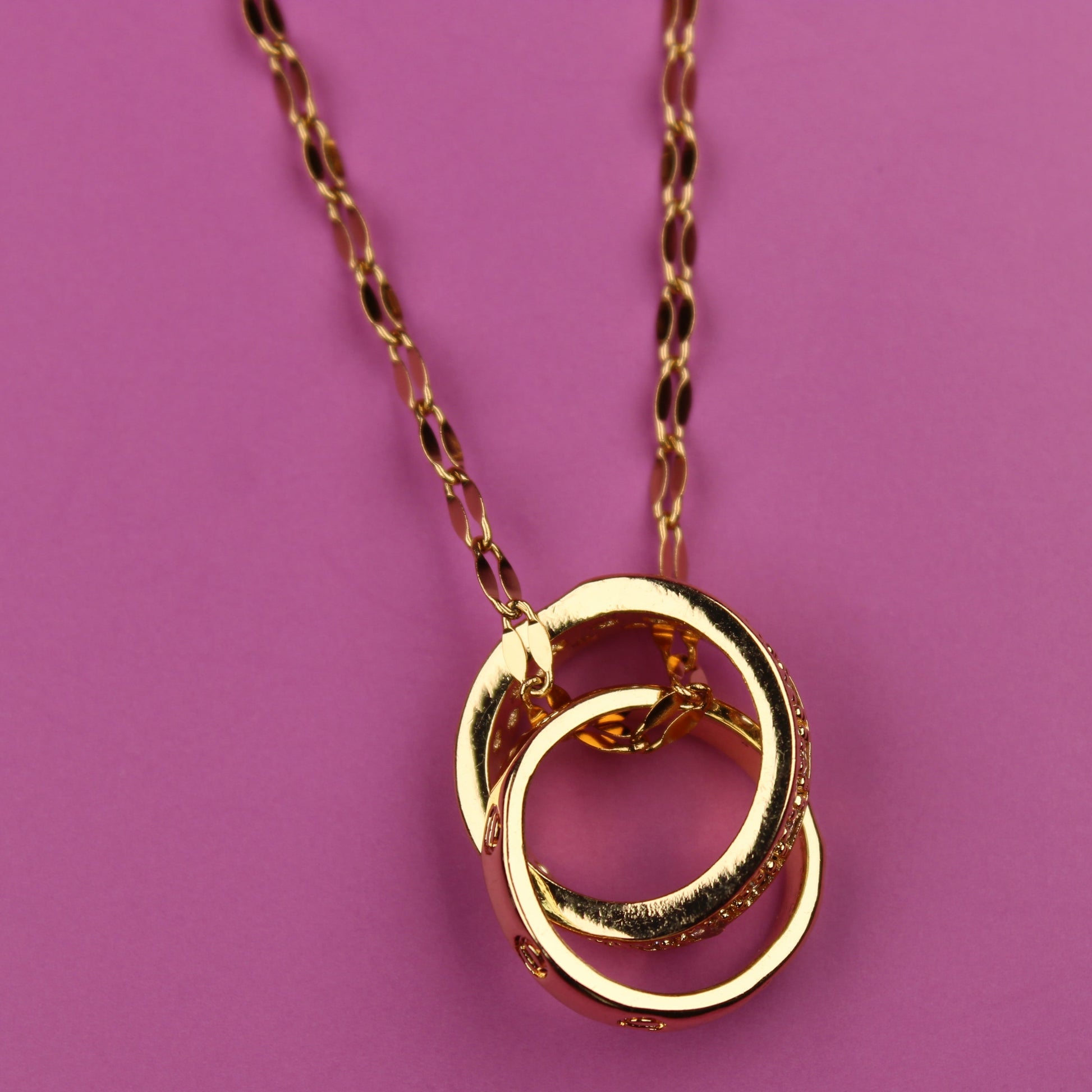 Gold necklace with interlocking rings on a pink background