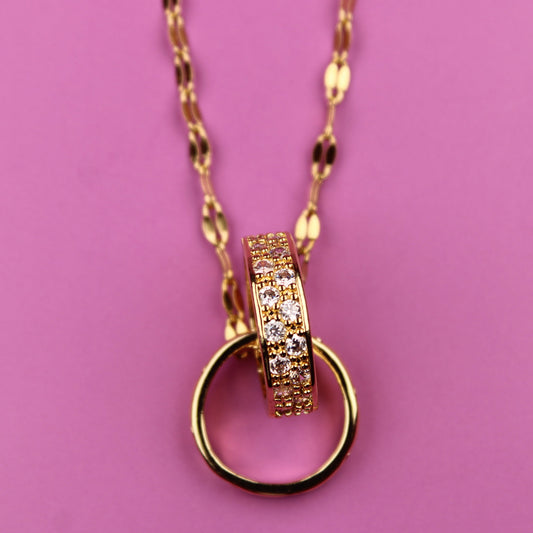 Gold necklace with a ring pendant on a pink background