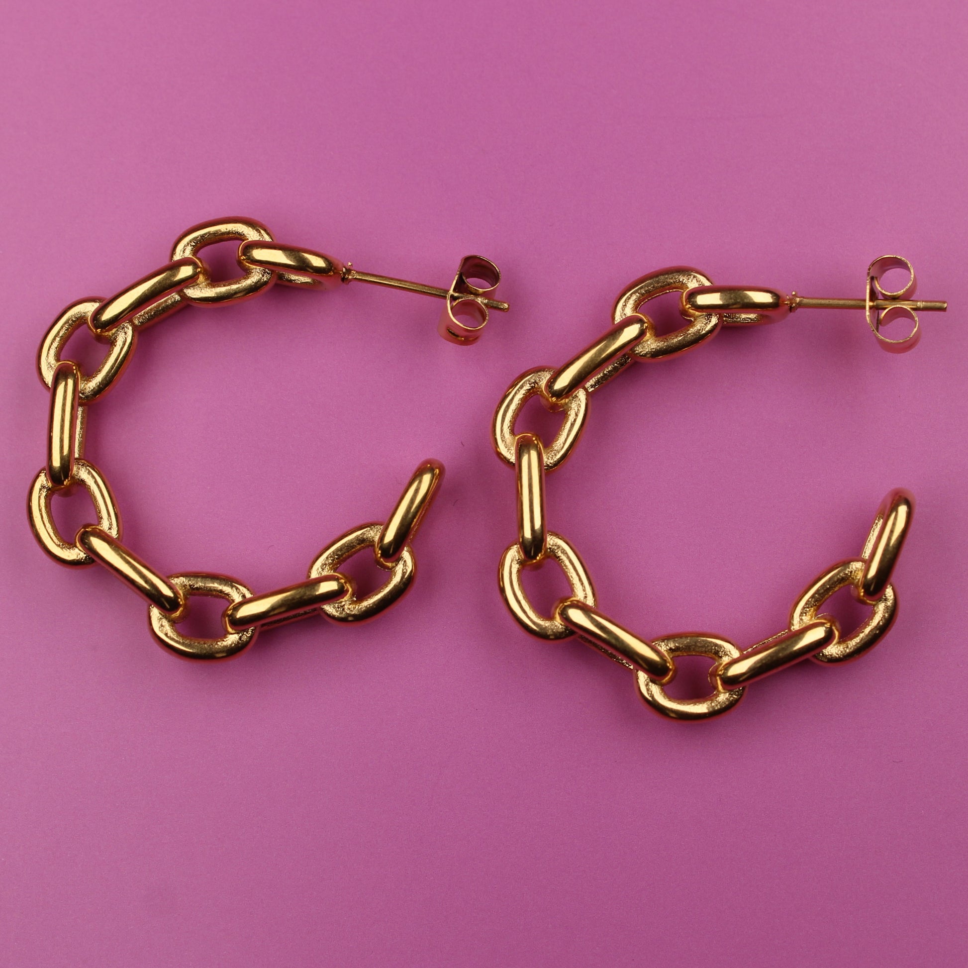 Gold chain hoop earrings on a pink background