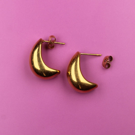 Gold crescent moon-shaped earrings on a pink background